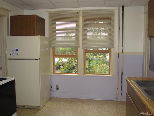 kitchen featuring freestanding refrigerator, electric stove, a drop ceiling, and a sink