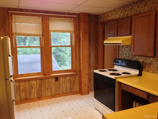 kitchen featuring under cabinet range hood, white appliances, light floors, and wood walls