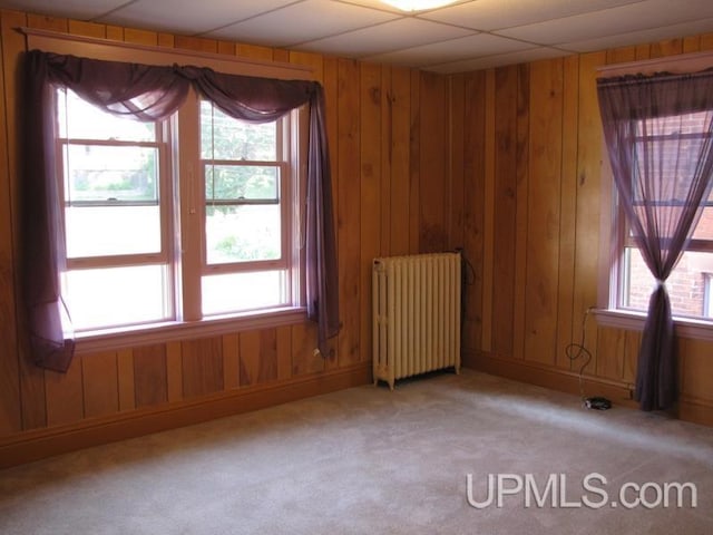 unfurnished room featuring radiator, light carpet, and wooden walls