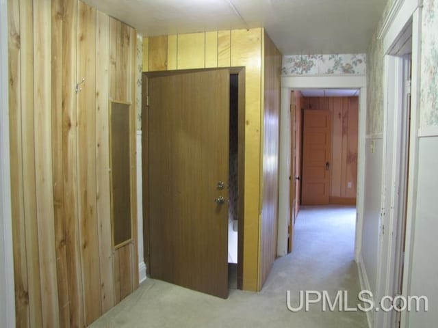 hall featuring light colored carpet and wooden walls