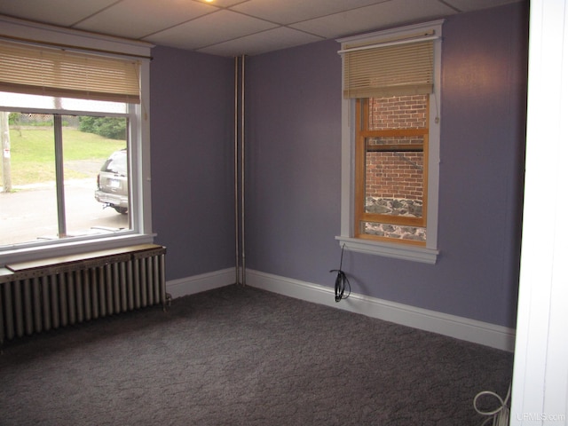 unfurnished room with carpet, baseboards, a drop ceiling, and radiator heating unit