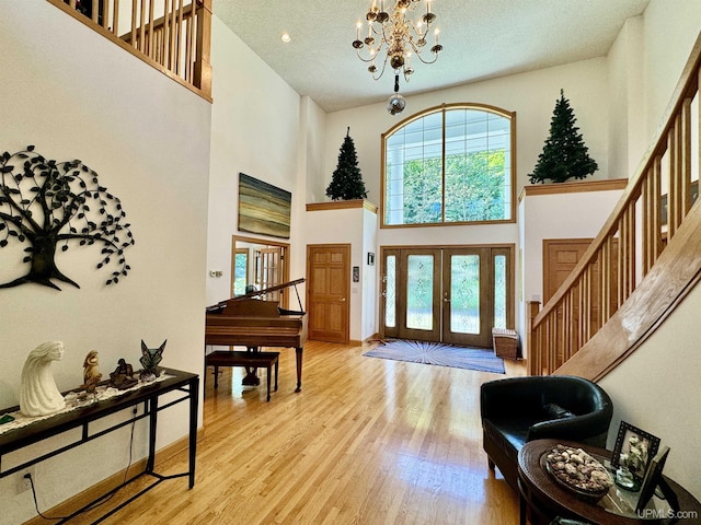 foyer featuring french doors, a high ceiling, light wood finished floors, a chandelier, and stairs