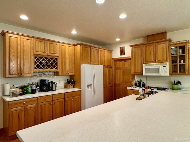 kitchen featuring recessed lighting, white appliances, brown cabinetry, light countertops, and glass insert cabinets