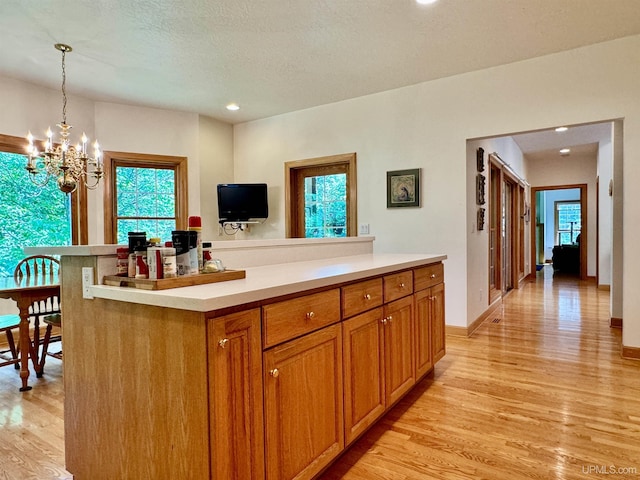 kitchen with brown cabinetry, light countertops, decorative light fixtures, light wood-type flooring, and a chandelier