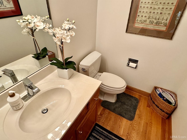 half bathroom with toilet, vanity, baseboards, and wood finished floors