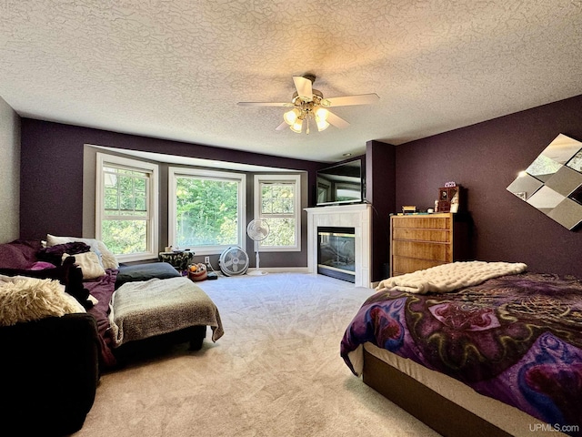 bedroom featuring a glass covered fireplace, a textured ceiling, carpet, and a ceiling fan