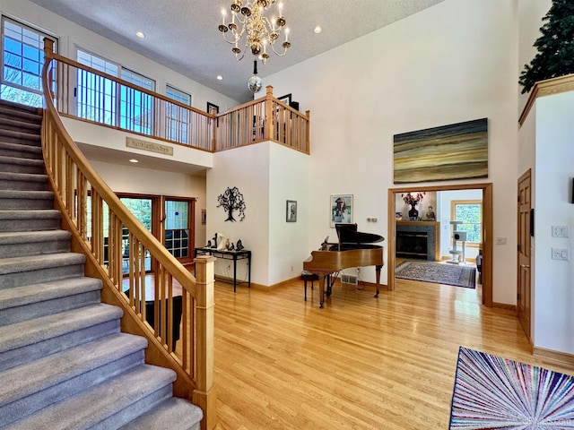 stairway with baseboards, a fireplace, a high ceiling, wood finished floors, and a notable chandelier