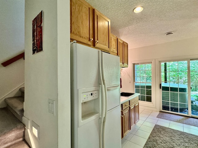 kitchen with light countertops, brown cabinets, white fridge with ice dispenser, light tile patterned flooring, and a textured ceiling