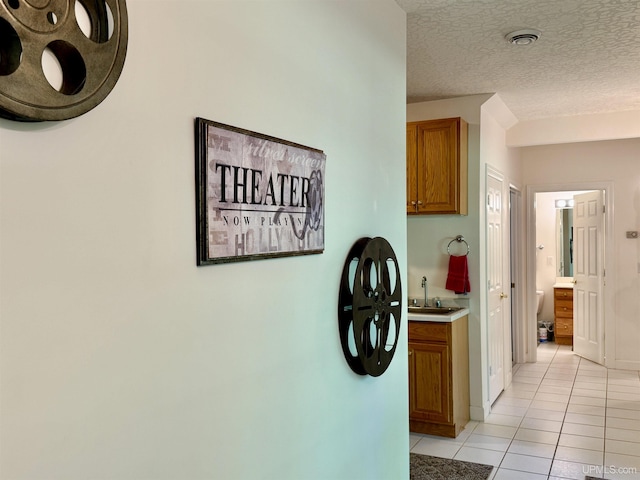 hallway featuring baseboards, visible vents, light tile patterned flooring, a sink, and a textured ceiling