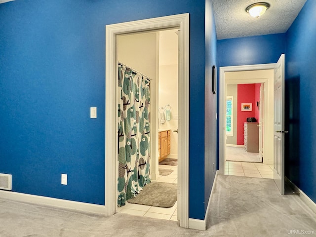 hallway with tile patterned floors, baseboards, carpet floors, and a textured ceiling