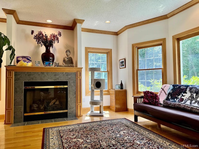 living area featuring a textured ceiling, wood finished floors, ornamental molding, and a tile fireplace