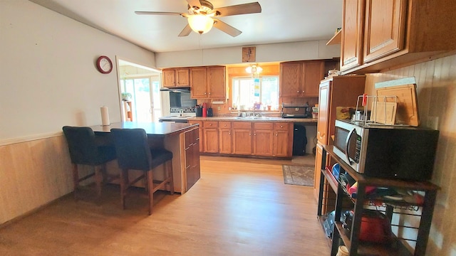 kitchen with a kitchen bar, sink, range with electric cooktop, ceiling fan, and light hardwood / wood-style floors