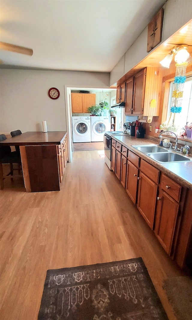 kitchen with light wood-type flooring, sink, washer and clothes dryer, and electric stove