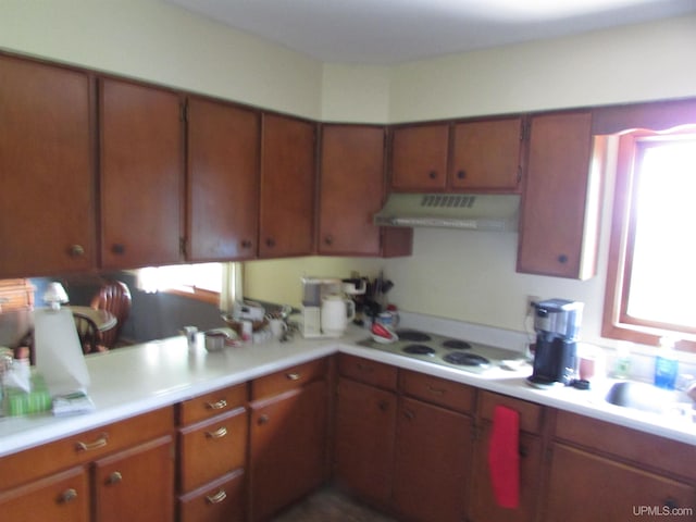 kitchen with light countertops, ventilation hood, brown cabinetry, and a sink