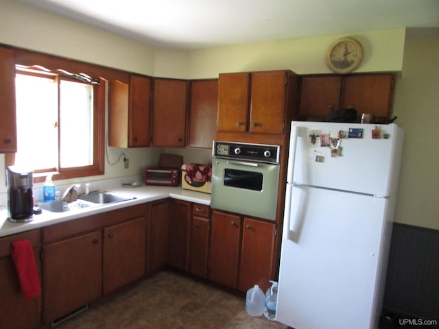 kitchen with brown cabinets, oven, freestanding refrigerator, light countertops, and a sink