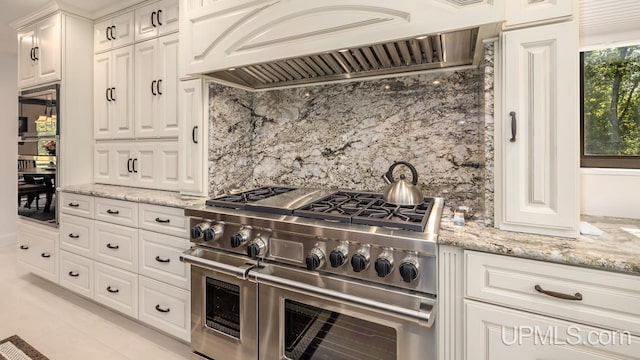 kitchen featuring range with two ovens, white cabinets, light stone counters, custom range hood, and backsplash