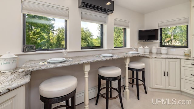 kitchen with white cabinetry, a kitchen bar, light stone countertops, an AC wall unit, and light tile patterned floors