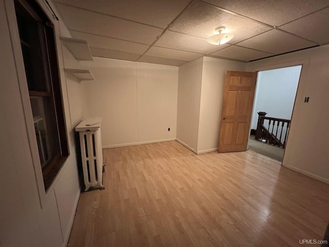 spare room featuring radiator heating unit, a paneled ceiling, and light wood-type flooring