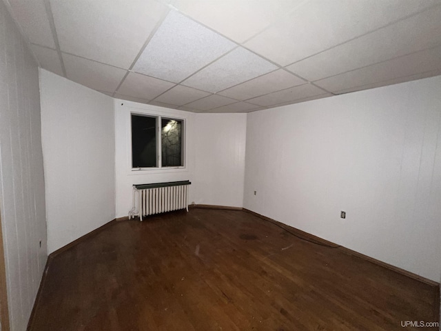 empty room featuring dark hardwood / wood-style flooring, radiator, and a paneled ceiling