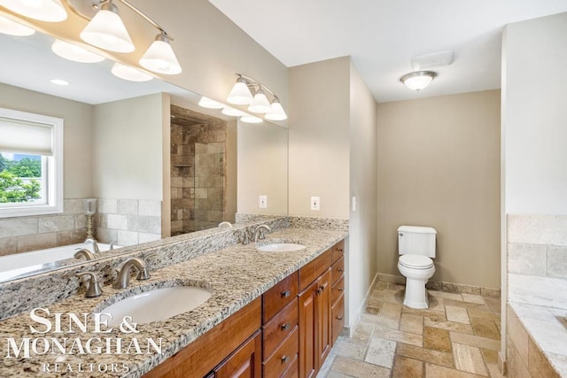 bathroom featuring tile patterned flooring, tiled bath, dual vanity, and toilet