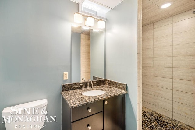 bathroom with vanity, tiled shower, and toilet