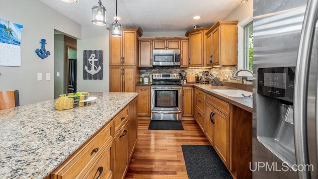 kitchen with appliances with stainless steel finishes, tasteful backsplash, sink, hanging light fixtures, and light stone counters