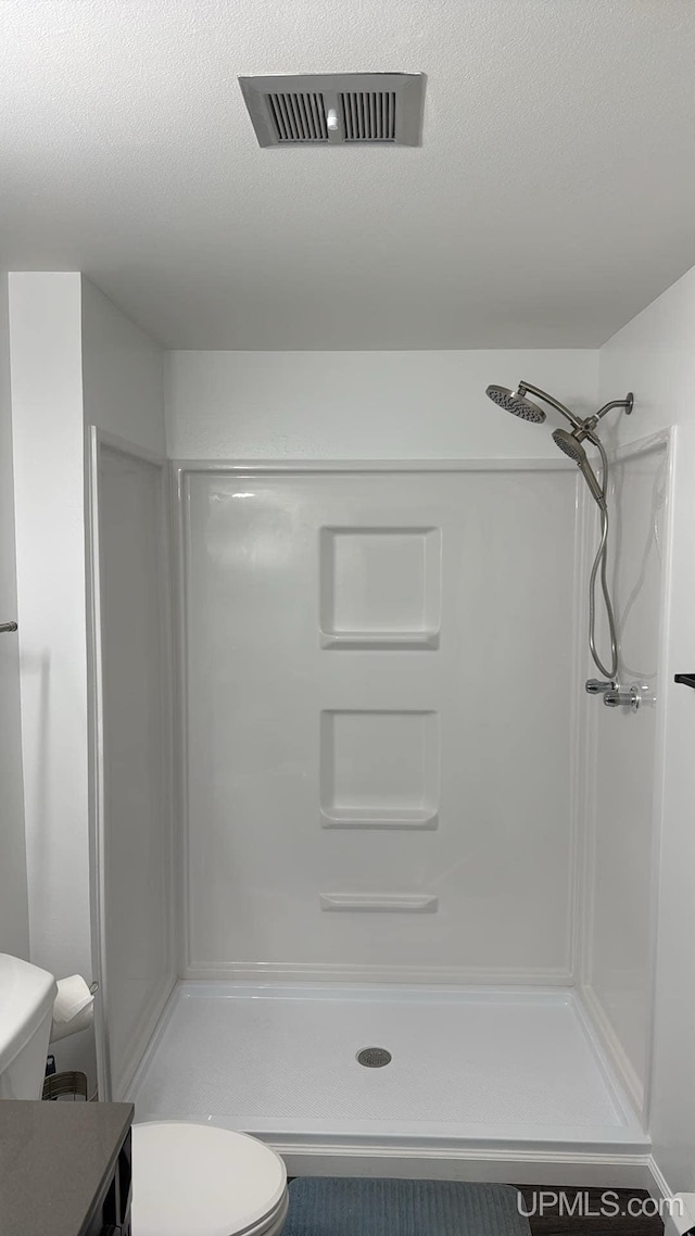 bathroom with a textured ceiling, a shower, and toilet