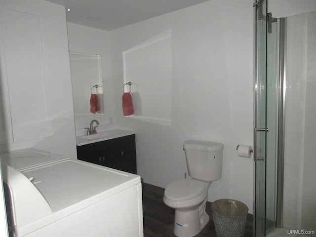 bathroom featuring washer / clothes dryer, a shower with shower door, toilet, vanity, and hardwood / wood-style flooring