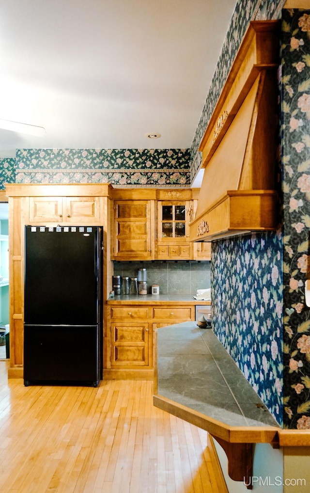 kitchen with premium range hood, black fridge, tasteful backsplash, light wood-type flooring, and tile counters