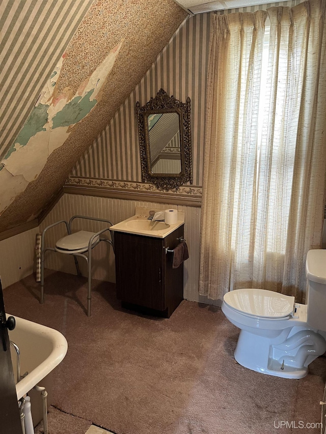 501 E N St, Ishpeming, MI 49849 - bathroom with wallpapered walls, toilet, wainscoting, vaulted ceiling, and vanity