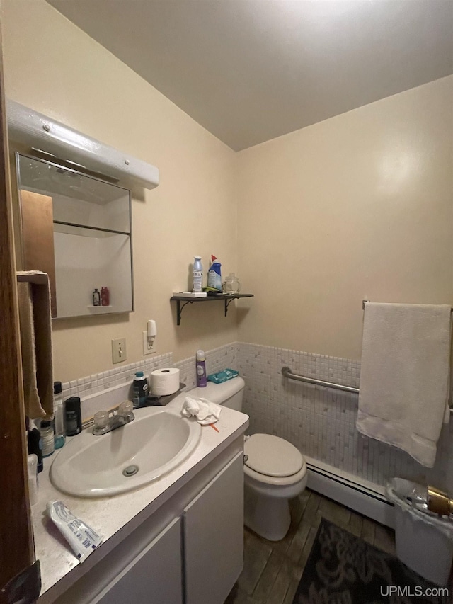 bathroom with tile walls, a baseboard heating unit, hardwood / wood-style floors, vanity, and toilet