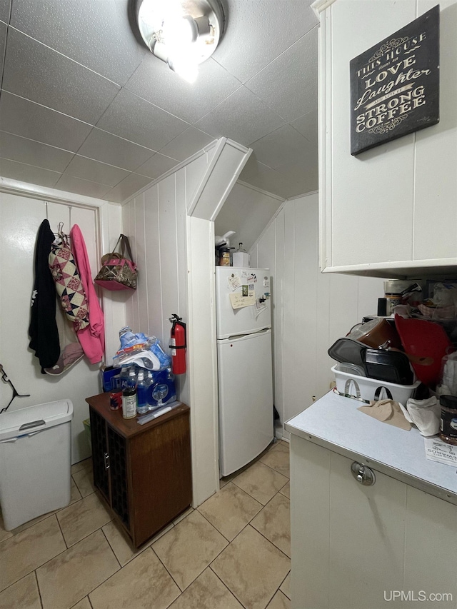 kitchen featuring white refrigerator, white cabinetry, wood walls, and light tile patterned floors