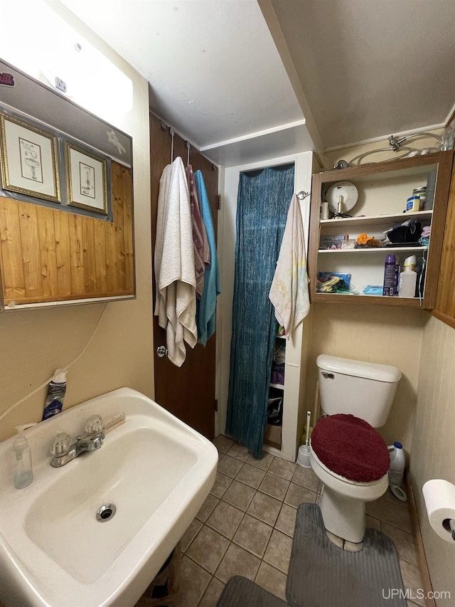 bathroom with tile patterned flooring, sink, toilet, and wood walls