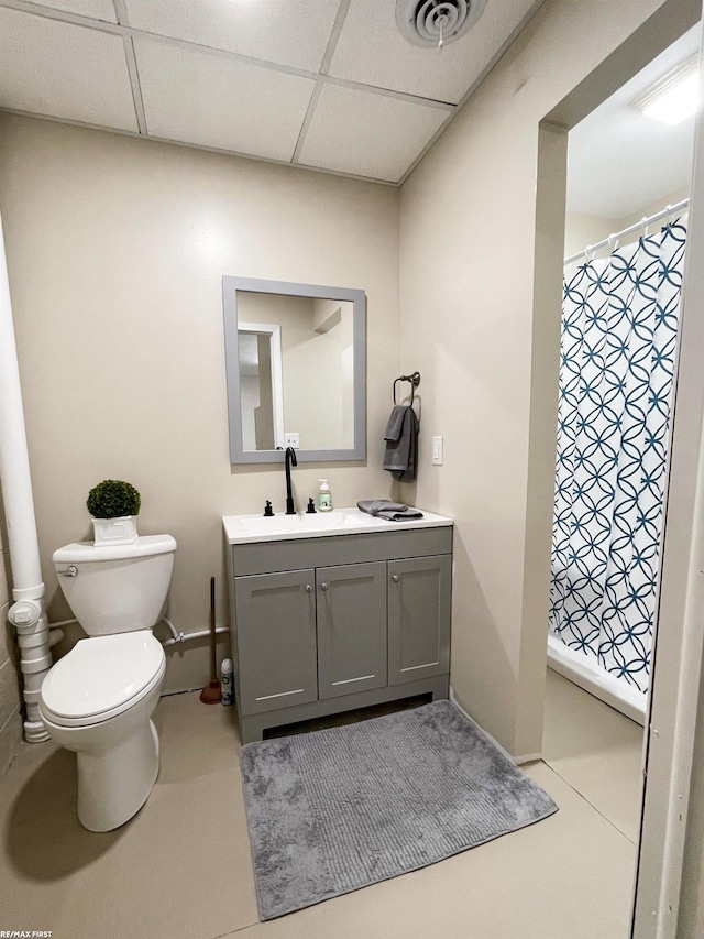 bathroom with vanity, toilet, a drop ceiling, and tile patterned floors