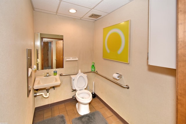 bathroom with toilet, a drop ceiling, tile patterned flooring, and sink