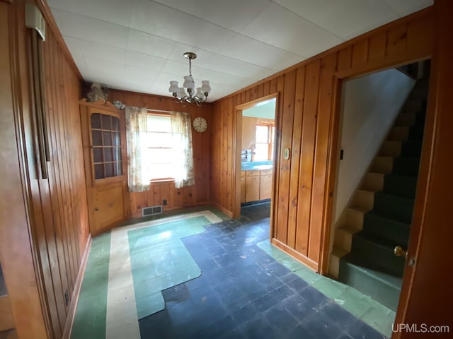 unfurnished dining area featuring tile patterned flooring, wood walls, and an inviting chandelier