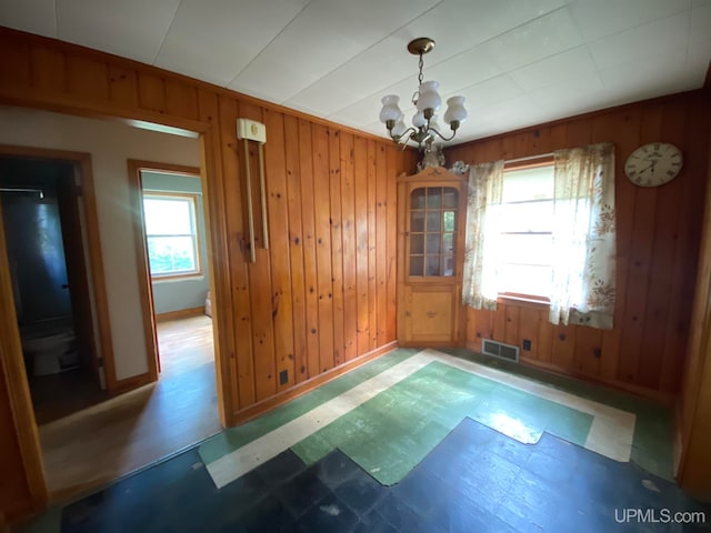 unfurnished dining area featuring a chandelier, wood-type flooring, wood walls, and a wealth of natural light