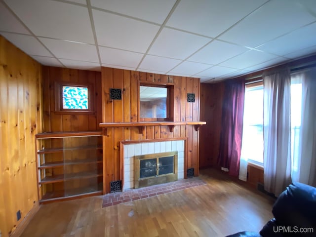 unfurnished living room featuring wood-type flooring, a drop ceiling, and wooden walls