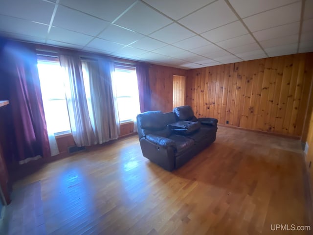 sitting room with wood walls, a paneled ceiling, and hardwood / wood-style floors