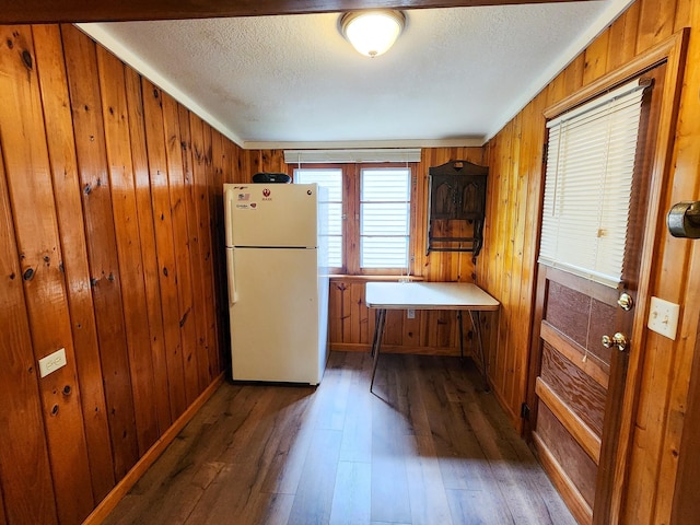 kitchen featuring brown cabinetry, wood walls, hardwood / wood-style floors, and freestanding refrigerator