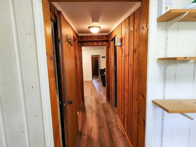 hall featuring wooden walls, light wood-style flooring, and a textured ceiling