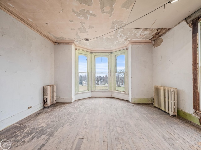 empty room with radiator heating unit, crown molding, and wood-type flooring