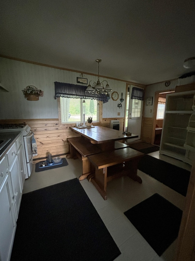 kitchen featuring wood walls, decorative light fixtures, white cabinetry, white gas stove, and an inviting chandelier