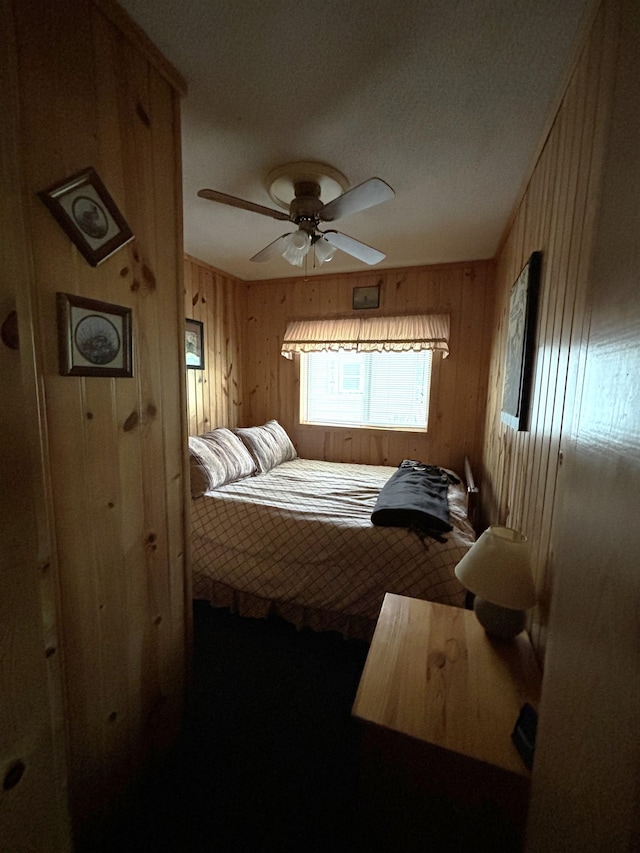 bedroom with a textured ceiling, ceiling fan, and wood walls