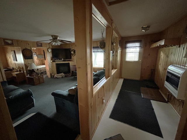 living room featuring heating unit, wooden walls, ceiling fan, and carpet flooring