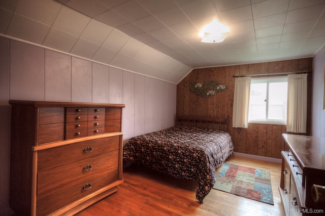 bedroom with wood walls, hardwood / wood-style flooring, and lofted ceiling