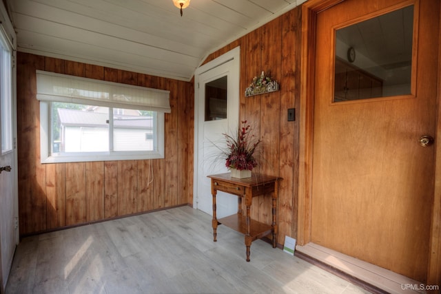 hall featuring lofted ceiling, light hardwood / wood-style floors, and wood walls