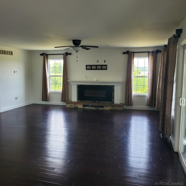 unfurnished living room featuring a wealth of natural light, visible vents, dark wood-type flooring, and a glass covered fireplace