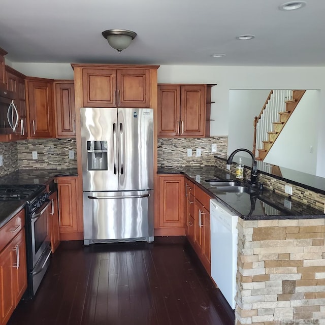 kitchen featuring stainless steel appliances, a sink, open shelves, dark stone countertops, and dark wood finished floors