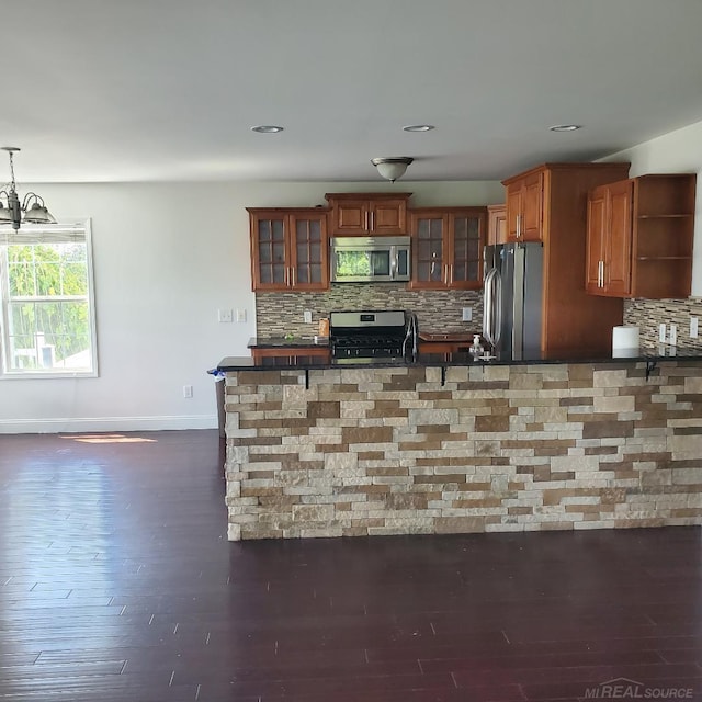 kitchen featuring appliances with stainless steel finishes, open shelves, brown cabinetry, dark countertops, and glass insert cabinets